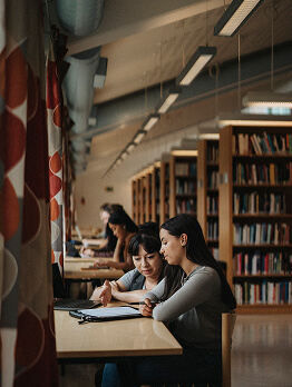 Studierende, die gemeinsam an einem Tisch in einer Bibliothek lernen.